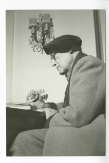 portrait photographique d’André Gide, avec lunettes et béret, assis, écrivant, chez Richard Heyd, hiver 1947